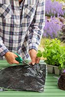 Woman cutting a circle out of black plastic with scissors to make hanging basket liner. 