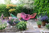 Relaxing seating area on a patio, enclosed by hedges and with a variety of container plantings 