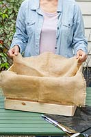Woman lining a wooden crate with hessian liner