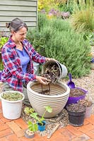 Woman adding a bucket of small twigs to large plastic planter