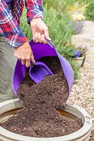 Woman adding fine garden compost to a large plastic planter