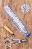 Large plastic bottle with base removed on wooden surface with bradawl and metal sissors