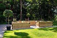 Raised vegetable beds made from modern wooden sleepers, on paved area near a lawn