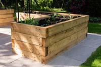 L-shaped raised vegetable bed made from modern wooden sleepers, on paved surface
