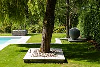 Modern garden, view over lawn with hard landscaped bed around specimen tree and and globe ornament