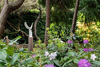 Barn owl sculpture on plinth, viewed through mature Rhododendron