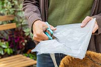 Woman using scissors to cut clear plastic to use as a liner for a hanging basket