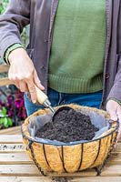 Woman filling lined hanging basket with compost