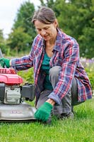 Woman adjusting the cutting height of a rotary lawnmower