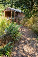 Pathway to the summerhouse, beds lined with various ferns, perennials and ornamental grasses including Stipa arundinacea