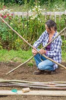 Woman using garden string to tie together two hazel poles