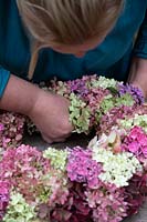 Woman inserting flower stem into woven wreath, fixing the flower to the base  and filling a gap