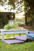 Table made out of a wooden pallet with central planter planted with mixed herbs in summer country garden with cushions