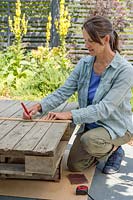 Woman using a piece of wood and a pencil to mark out a cutting line on a wooden pallet