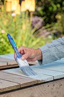 Woman using a paint brush to apply a pastel coloured outdoor paint to wooden table. 