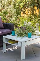 Wooden pallet table with intergral sunken planter, with summer planting on slate patio in summer, accompanied by outdoor chairs.
