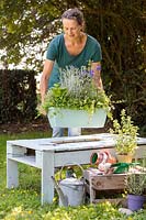 Woman inserting a plastic trough planted with herbs, into a wooden table. 