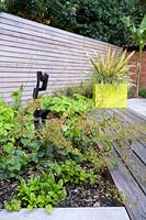 Small Modern Garden with Phormiumin in yellow pot and planting of Heuchera, Epimedium and ferns in bed