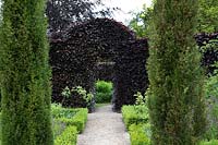 View through pair of Taxus - Fastigiate Yew - to different types of hedging: Fagus sylvatica - Beech hedge with arch and Buxus - Box - edging around beds 