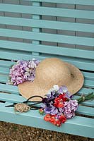 Lathyrus odoratus - Bunch of cut sweet pea flowers and sun hat on a garden seat.
