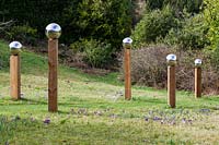 Avenue of wooden columns topped with stainless steel globes in the Meadow. Crocus in grass. 