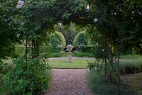 Rosa 'AlbÃ©ric Barbier'- Rambling Rose around arch with view to stone urn 