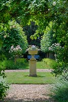 Stone urn on plinth in centre of romantic formal country garden, June