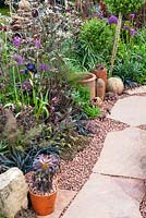 Stone path with granite chips alongside border of mixed plants and garden bric-a-brac - RHS Malvern Spring Festival