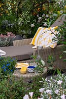 Wicker lounger with cushions and table in sheltered garden area  - RHS Chelsea Flower Show