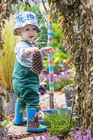 Young toddler holding a pine cone in sensory garden