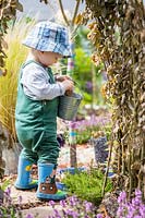 Young toddler putting items into a metal bucket in sensory garden