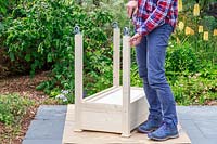 Woman using a screwdriver to attach small casters to the legs of a raised wooden planter