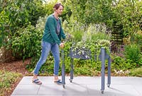 Woman pushing a raised wooden planter on casters across a patio