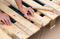 Woman fitting cut pieces of narrow wood to fill gaps in pallet. 