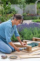 Woman using an electric screwdriver to fix planks on to the sides of the pallet to hide the planting trays. 