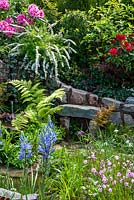 Raised border of shrubs including Rhododendrons,  Spirea and Dogwood above water outlet from natural spring, feeding into a stream edged with Ferns, Fritillaria meleagris, Lychinis flos-cuculi 'Petite Jenny' and Camassia leichtlinii - RHS Malvern Spring Festival