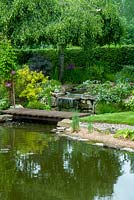 Small waterfall between garden pools with foot bridge, shrubs and marginal plants - Open Gardens Day, Bures, Suffolk