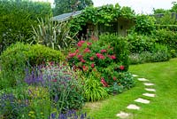 Summer border of Lavenders, Rose Campions, Verbena, Grasses, Rose bush, Phormium, Cranesbill Geraniums and various shrubs with stepping stones leading to vine covered summerhouse - Open Gardens Day, Kelsale, Suffolk