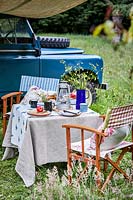 Table and chairs set for picnic, landrover in background