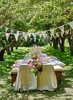 Summer table setting in orchard with central floral arrangement and bunting 