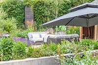 View under parasol to patio with lounge furniture surrounded by flower beds