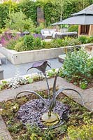 View across modern metal water sculpture to sunken garden with raised beds  and seating area