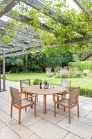 Patio and metal pergola with climbers running along house, edged with Buxus hedging, wooden dining furniture