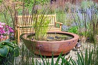Corten steel pond and wooden bench  surrounded by mixed planting