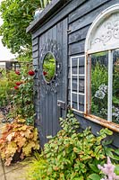 Shed painted black and decorated with mirrors to reflect light into the garden