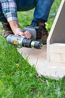 Man using an electric drill to predrill holes for fixing end triangle to sides
