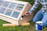 Man painting coldframe using a paint brush