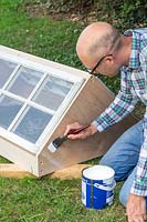 Man painting coldframe using a paint brush