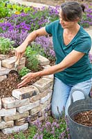 Woman using a scoop to add wood chippings as a mulch to herb spiral