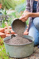Woman adding grit to compost in a glavanised container